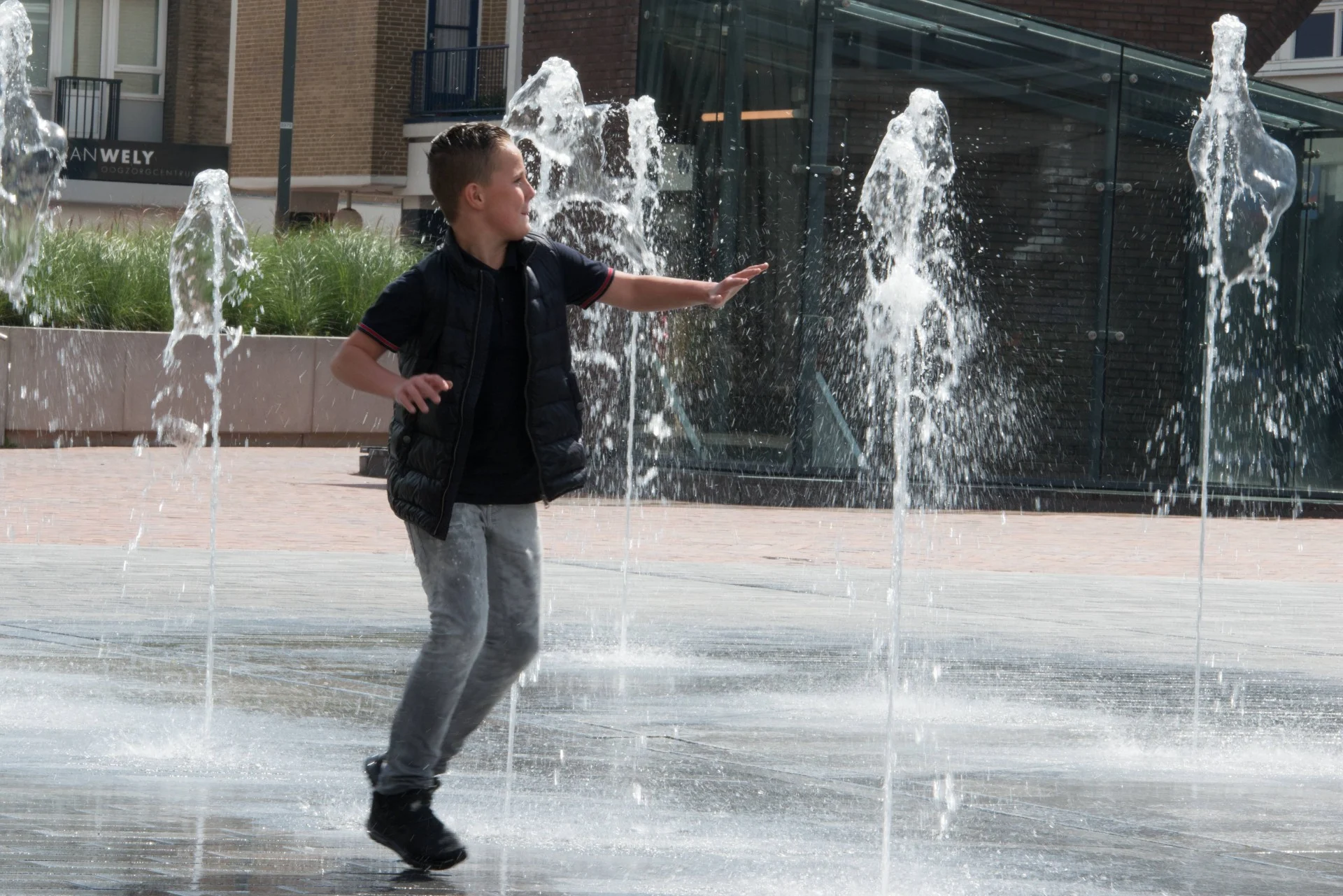 fontein fonteinen aanleg realisatie aannemer maken bouwen plein gemeente stad aannemerij leverancier waterkunstwerken fonteintechniek natuursteen (28) Een jongen speelt tussen de fonteinen op de Nieuwe Markt in Roosendaal