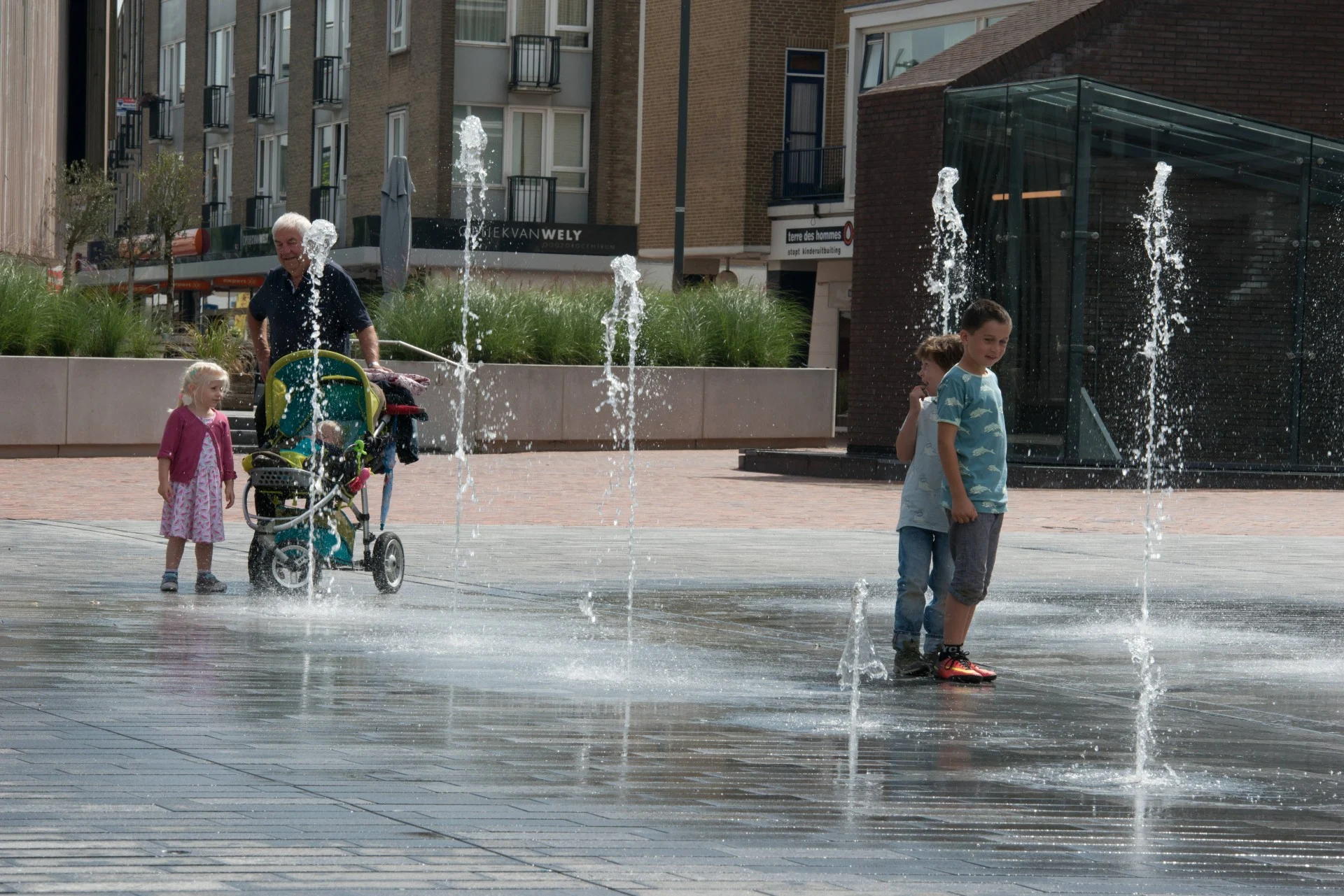 fontein fonteinen aanleg realisatie aannemer maken bouwen plein gemeente stad aannemerij leverancier waterkunstwerken fonteintechniek natuursteen (31) Peuters en een opa kijken naar de fonteinen op de Nieuwe Markt in Roosendaal