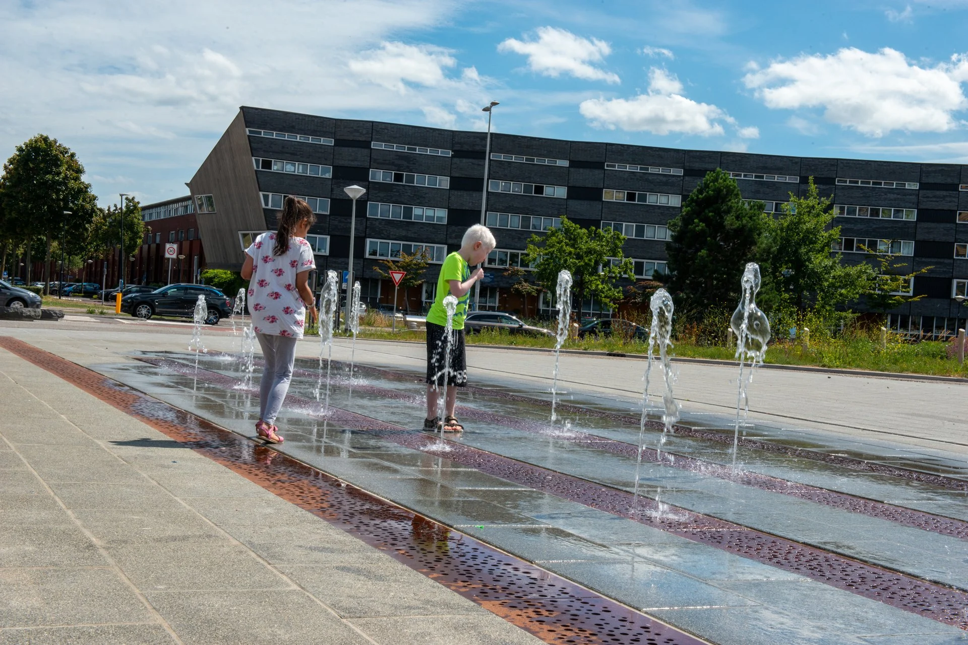 20250621 244 Zutphen Noorderhaven RM Twee kinderen spelen bij de fonteinen op het Ecuplein in Amsterdam, naast een cortenstalen goot