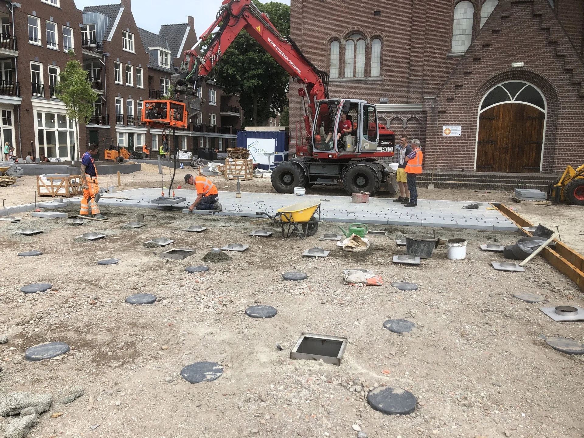 Een graafmachine en medewerkers leggen de bestrating en plaatsen spuiters op het Kerkplein in Hoogeveen