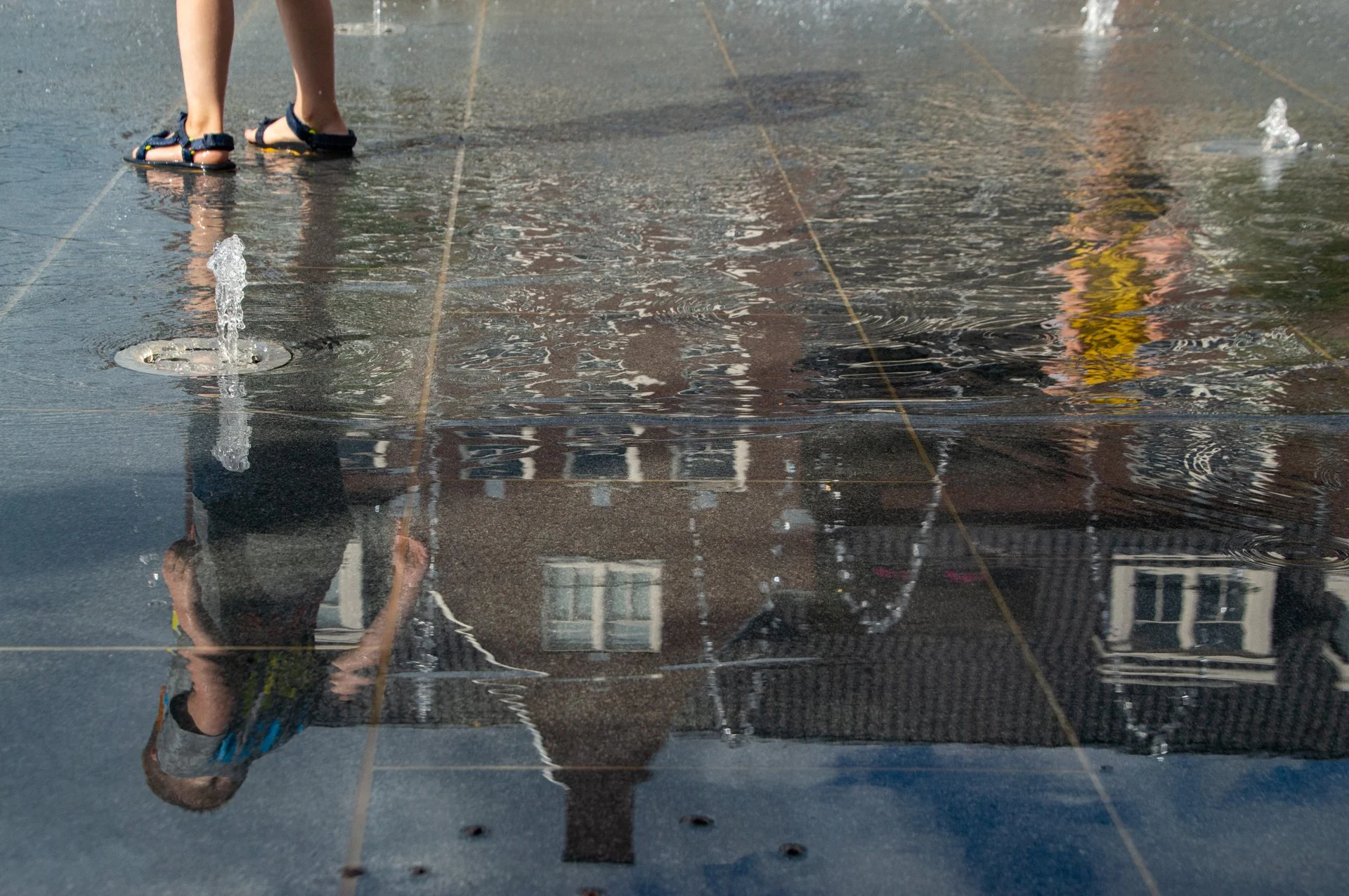 Het spiegelbeeld van een kind en de gevels in het natte plein in Hoogeveen