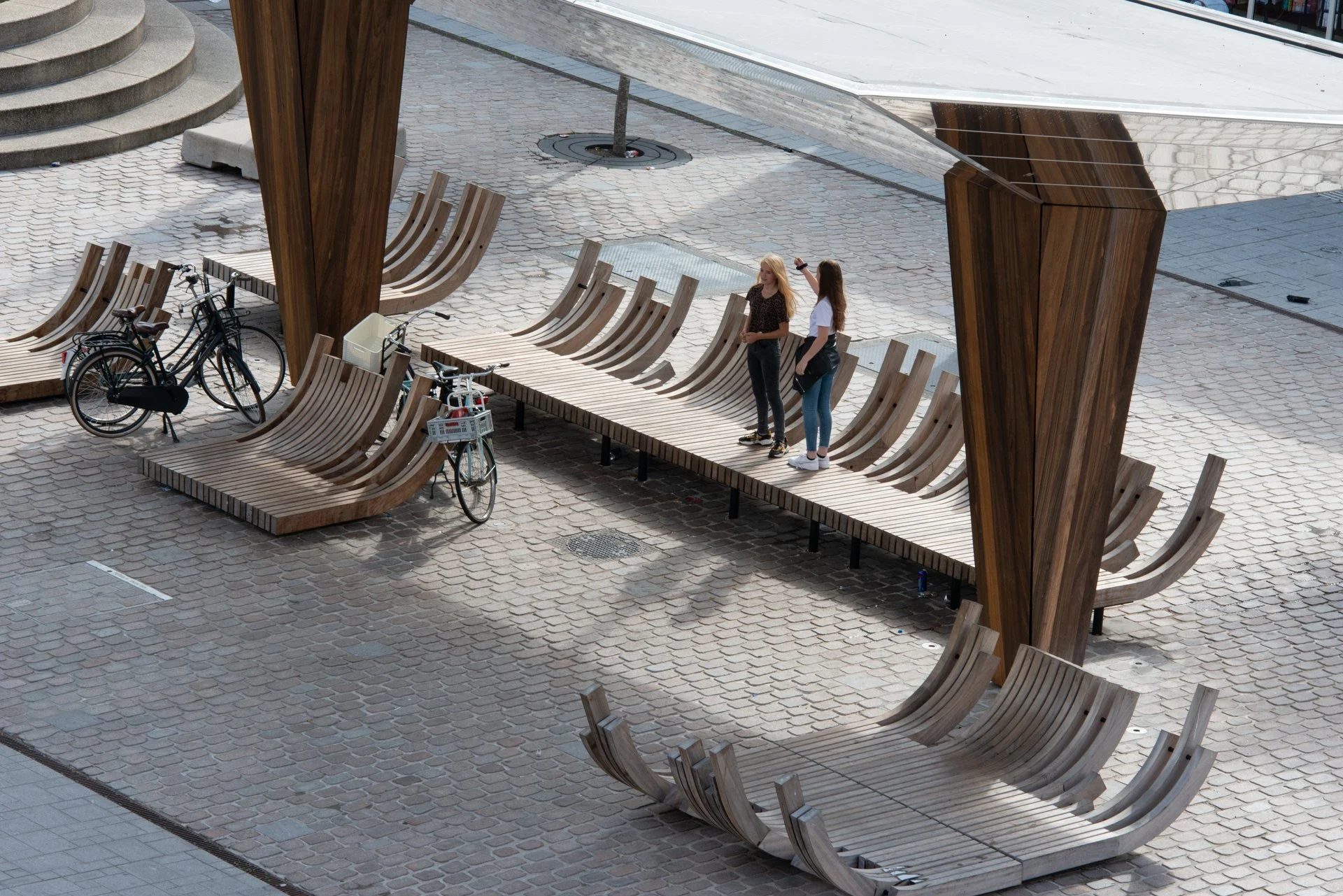 Twee mensen bij de houten loungebanken onder de spiegelkraan op het Kerkplein in Hoogeveen