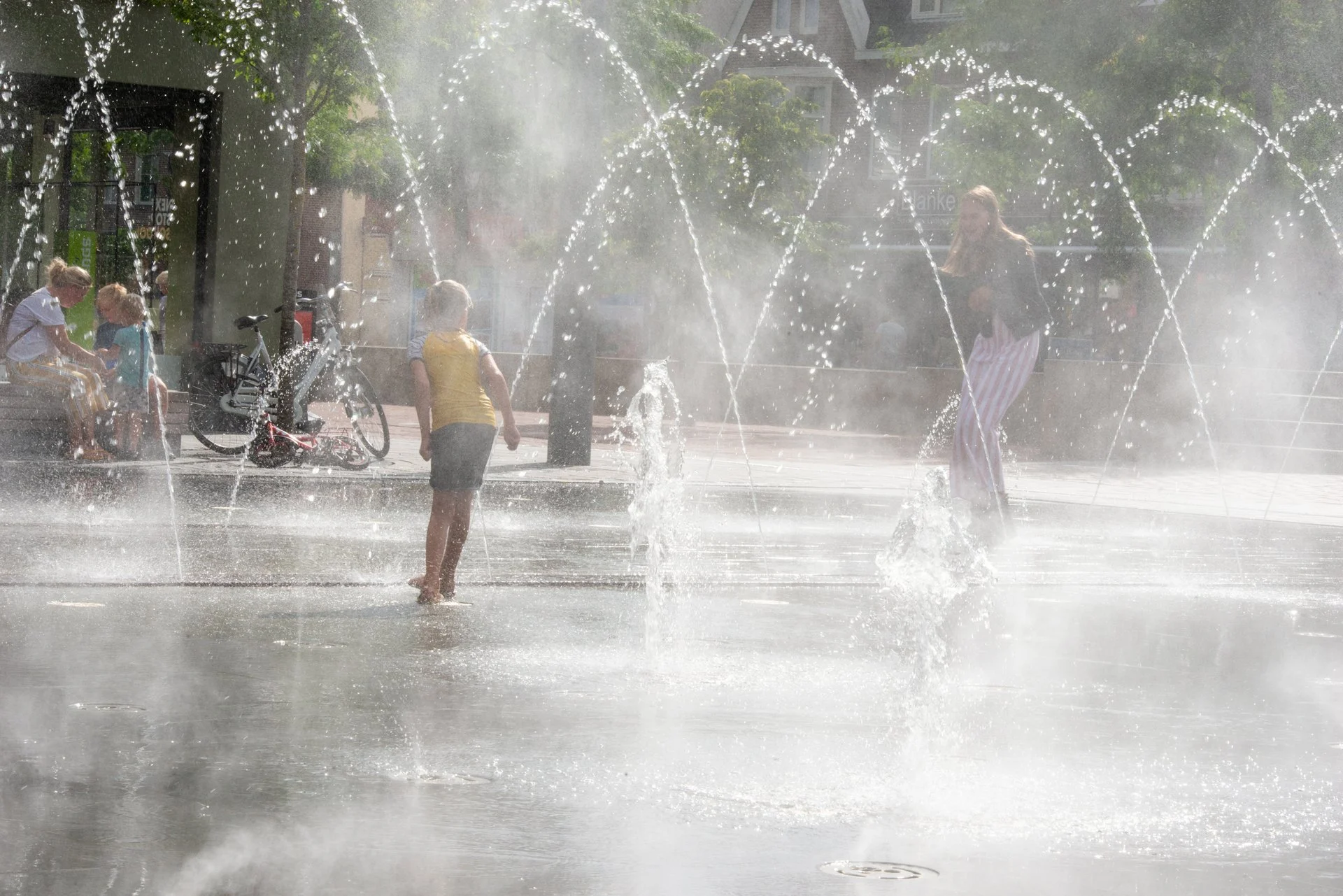 Kinderen spelen tussen de waterbogen van de fonteinen op het Kerkplein in Hoogeveen