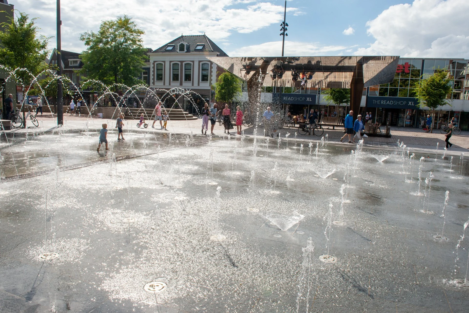Overzicht van het fonteinplein met spelende kinderen en waterbogen op het Kerkplein in Hoogeveen