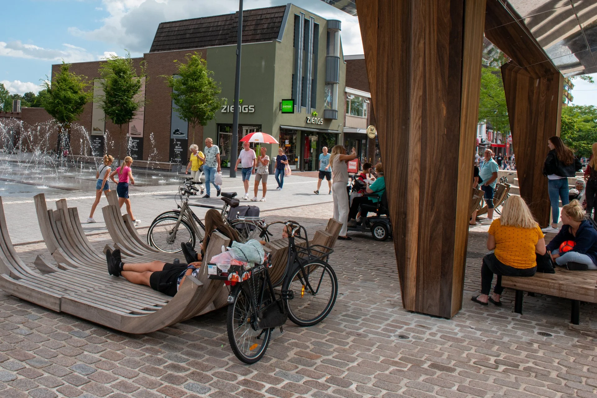 Mensen zitten op de loungebanken onder de spiegelkraan op het Kerkplein in Hoogeveen