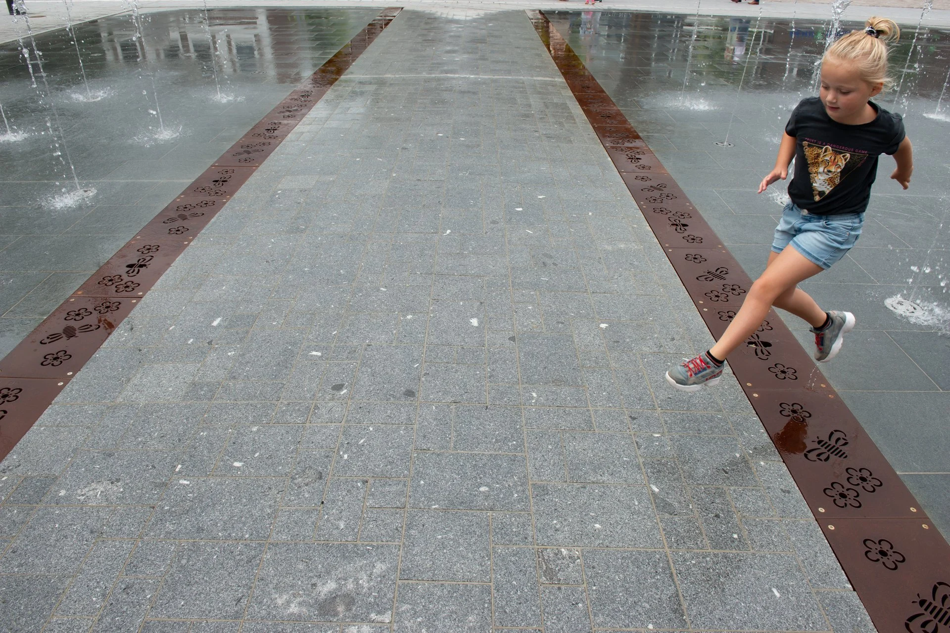Een meisje springt over het spiegelvlak met een cortenstalen strip op het Kerkplein in Hoogeveen