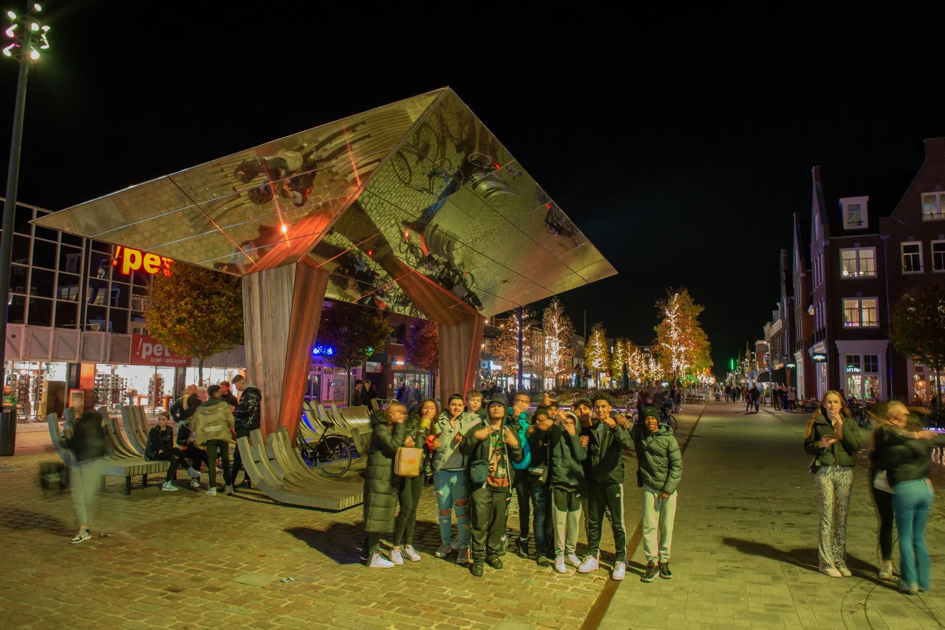 Een groep mensen onder de spiegelkraan op het Kerkplein in Hoogeveen in de avond