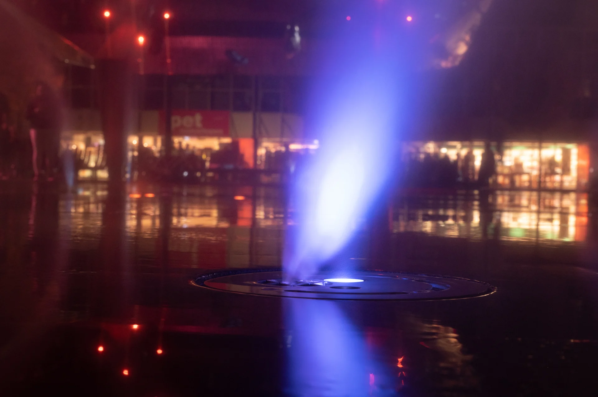 Een blauw verlichte fontein in het donkere spiegelvlak op het Kerkplein in Hoogeveen